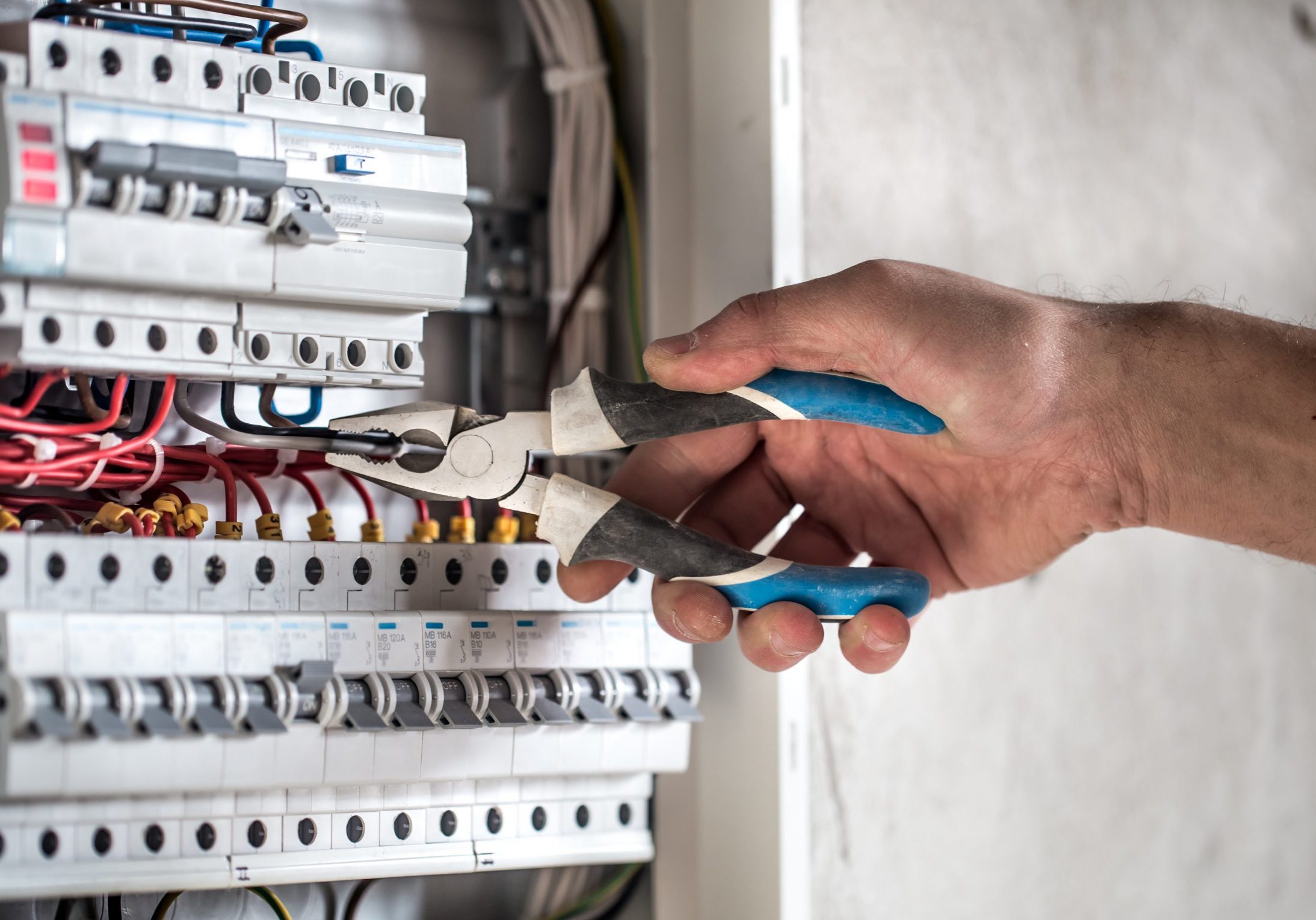 Man, an electrical technician working in a switchboard with fuses. Installation and connection of electrical equipment. Professional with tools in hand. concept of complex work, space for text.